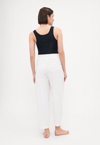 Zwarte tanktop en witte textuurbroek met een subtiel patroon, voorzien van een losse pasvorm en een elastische tailleband. Achteraanzicht.