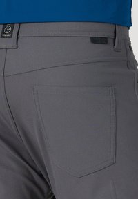 Nahaufnahme von hinten einer Person, die graue Wrangler ATG Outdoor-Hosen und ein blaues Hemd trägt, mit Fokus auf das Gesäßtaschen- und Taillenbandetikett.