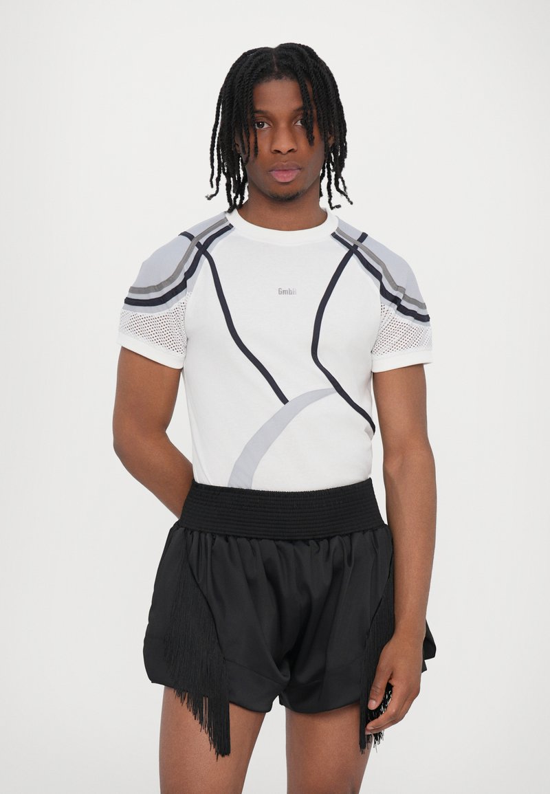 Hvid kortærmet skjorte med grå accenter og meshskulder, parret med sorte shorts med frynse-detaljer og en smocket talje.