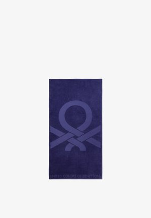 Serviette bleu foncé avec un grand motif de ruban bouclé au centre et le texte « United Colors of Benetton » en bas.