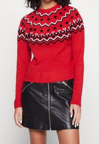 Czerwony sweter z dzianiny o geometrycznym wzorze w czerni i bieli, z długimi rękawami i okrągłym dekoltem, w połączeniu z czarną skórzaną spódnicą.