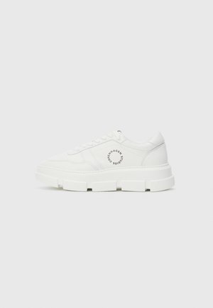 Witte lage sneaker met een robuste zool, gestikte details, veters en een circulair "Copenhagen Studios" logo aan de zijkant tegen een egale achtergrond.