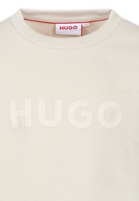 Sweatshirt beige chiaro con tessuto a maglia testurizzato, scollo rotondo e la parola incisa "HUGO" in evidenza sulla parte anteriore.
