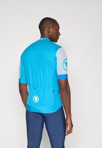 Maillot de cyclisme bleu à manches courtes, design ajusté, tissu texturé et poche arrière. Présente un logo sur la manche et l'ourlet inférieur.