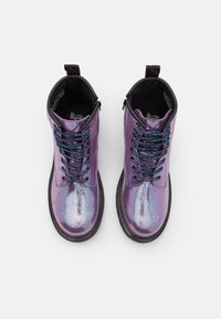 Botas de tobillo moradas con una textura brillante y holográfica. Presentan acentos negros, cordones texturizados y una suela resistente con lengüeta en el talón.