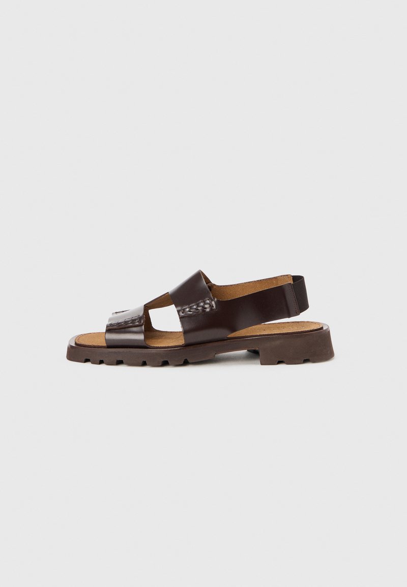 Sandalo marrone in pelle con suola piatta, design a fasce incrociate e soletta imbottita; presenta dettagli cuciti e cinturino sul tallone per supporto.