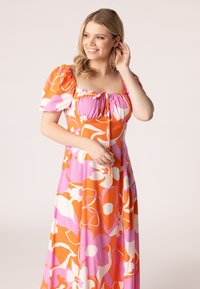 Maxi jurk in een oranje en roze bloempatroon, met pofmouwen en een vierkante halslijn met trekkoord-detail. Zachte fabric textuur.