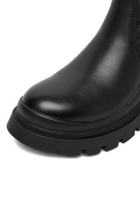 Czarne skórzane botki do kostki z okrągłym noskiem, grubą teksturowaną podeszwą oraz starannie wykończonymi szwami wzdłuż boku. Gładkie wykończenie o matowym wyglądzie.