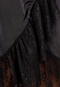 Un tissu noir avec une finition satinée lisse comporte une bordure en dentelle superposée. La dentelle présente des motifs floraux complexes et des bords festonnés.