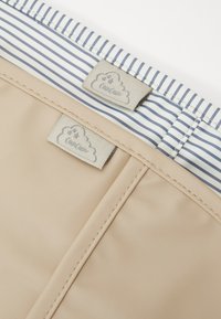 Tissu beige au toucher lisse, avec un intérieur doublé de rayures bleu et blanc, et deux étiquettes grises avec un logo de nuage.