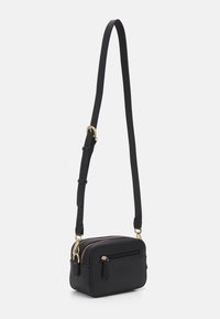 Malá černá crossbody taška s nastavitelným popruhem, zlatými kovovými detaily, přední zipovou kapsou a dvěma hlavními zipovými oddíly.