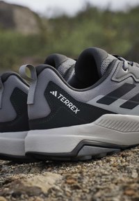 Close-up of gray and black Terrex trail running shoes on gravel outdoors, showing textured soles and mesh upper.