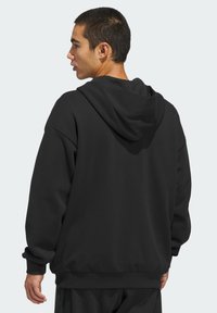 Crna pamučna majica s kapuljačom s prostranom kapuljačom, opuštenim krojem, rebrastim manšetama i donjim rubom. Glatka tekstura i minimalistički dizajn bez ukrasa.