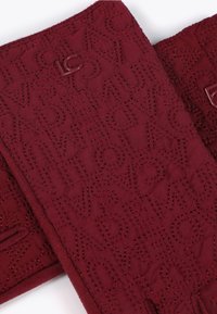 Burgundijska kviltana tkanina s urezanim tekstom po cijeloj površini. Glatka tekstura s toniranim šavovima i malim metalnim logotipom.