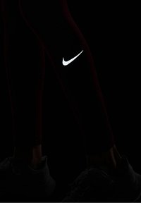 Svarta leggings med en åtsittande design, prydda med en framträdande vit Nike-logotyp på vänster lår och kombinerade med grå träningsskor.