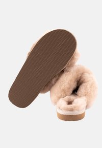 Pantofole in pelle di pecora beige con una texture morbida e soffice, soletta imbottita e suola in gomma con una presa a motivo.