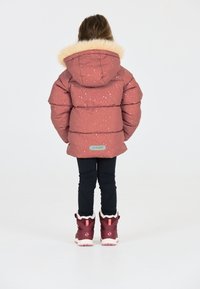 Polstret pink jakke med hvide prikker og en faux fur hætte, parret med mørke leggings og burgunder vinterstøvler med hvidt foer.