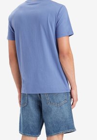 Camiseta de manga corta azul hecha de una tela suave, combinada con shorts de mezclilla descoloridos que cuentan con bolsillos traseros y un dobladillo sin rematar.