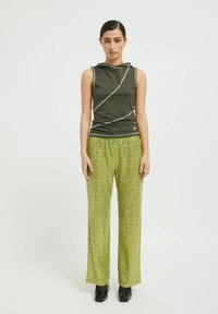 Olivno zelena brezrokavna majica z belimi detajli; ohlapne svetlozelene hlače s sekvincami in teksturiranim vzorcem; črne platforme.