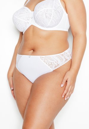 Plus-size vrouw die een witte beha van kant en effen stof draagt, met bijpassende hoog uitgesneden slipjes, staand tegen een witte achtergrond.