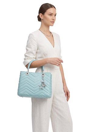 Donna con abito bianco che tiene una borsa trapuntata azzurro chiaro con ciondoli a forma di stella in argento sul manico.