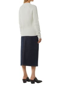 Pull blanc à côtes avec des manches longues, associé à une jupe midi en denim foncé avec une couture centrale, et des chaussures à talons carrés noires.