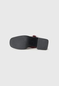 Red leather shoe with a wide black rubber sole, featuring a square toe design and a low, block heel. The underside is textured for grip.
