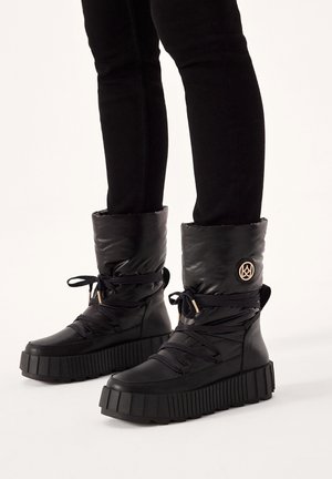 Schwarze Stiefel mit einem gepolsterten Schaft und dicken, geriffelten Sohlen. Mit Schnürsenkeln, einem Logo-Akzent und einem wasserdichten Design für kaltes Wetter.