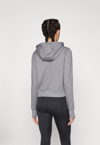 Grau gekürzter Hoodie mit Kapuze, gerippten Bündchen und Saum; glatte Textur. Getragen mit schwarzen Leggings, die einen körperbetonten Sportstil zeigen.