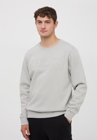 Felpa grigia chiara con colletto rotondo, con lettering testurizzato "REALITY" sul davanti e polsini e orlo a costine. Texture del tessuto morbida.