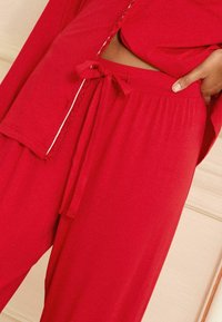 Rød 2-delt loungewear sæt med bånd i taljen på bukserne og korte ærmer med dekorativ syning på toppen. Blød tekstur.