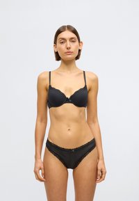 Mustast pitsist pesukomplekt, mis sisaldab pitsäärtega rinnahoidjat reguleeritavate rihmadega ja sobivaid pitsdetailidega pitskanga aluspükse, siledast materjalist ja pehme tekstuuriga.