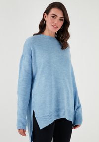 Gaiši zilas pārāk liela izmēra džemperis, kas izgatavots no mīksta adījuma auduma. Tam ir ribota apkakle un aproces, kā arī sānu izgriezumi brīvākai piegrieztai formai.