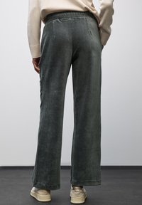 Pantalons larges en velours côtelé vert foncé, dotés d'une taille élastique et de poches arrière épurées. Associés à des baskets beiges.