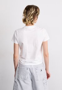 White cotton t-shirt with a rounded neckline and short sleeves, worn with gray cargo pants featuring large pockets and stitching details.