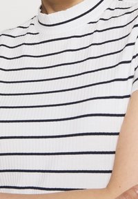 Top de rayas acanalado en blanco y azul marino, con cuello alto y mangas cortas, fabricado en un tejido texturizado y con rayas horizontales uniformes.