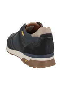 Donkerblauwe suède en leren sneaker met een beige kraag, witte tussenzool en bruine rubberen buitenzool. Gele accent boven de hak.
