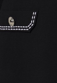 Tissu noir à finition texturée, avec une poche ornée de coutures blanches et d'un bouton-pression argenté.