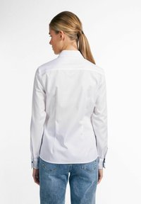 Witte overhemd met gestructureerde kraag, lange mouwen met knoopmanchetten en een getailleerde pasvorm, gecombineerd met lichtblauwe jeans.