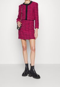 Rosa tweed-jacka och kjolset med svarta accenter, prydd med guldknappar och fickor med dragkedja. Kombineras med svarta kraftiga ankelstövlar.