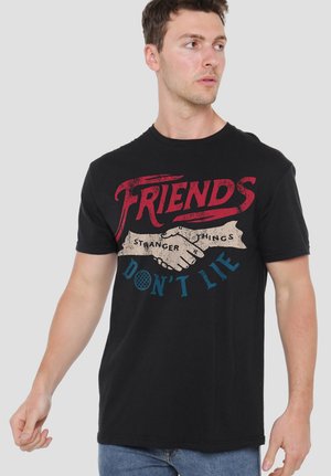 Man wearing black t-shirt with red and blue "Friends Don't Lie" text and handshake graphic, referencing Stranger Things series.