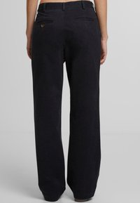 Black wide-leg trousers made of cotton, featuring back pockets with button detail. Smooth texture, tailored fit, and ankle-length design.