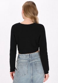 Suéter negro corto con mangas largas y tela de punto texturizada. Presenta un escote con un diseño en forma de onda. Combinado con una falda de mezclilla azul claro.