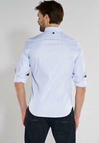 Hellblaues, gestreiftes Button-Up-Hemd mit klassischem Kragen und hochgerollten Ärmeln, versehen mit schwarzen Akzenten und einem abgerundeten Saum.