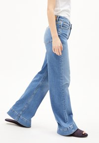 Lichtblauwe, wijdvallende jeans met een klassiek vijf-pocket ontwerp en een rafelige zoom, gecombineerd met donkerpaarse slidesandalen.