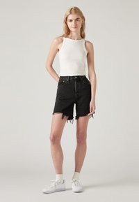 Black denim high-waisted shorts with frayed hem, paired with a white fitted tank top. Accessories include white sneakers and ankle socks.