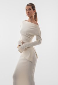 Maglione a costine crema con design scollato e maniche lunghe, abbinato a una gonna coordinata con uno spacco laterale e una silhouette fluida.
