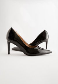Zapatos de tacón alto de charol negro con punta afilada, tacón de aguja delgado y superficie lisa; con un diseño minimalista y elegante.