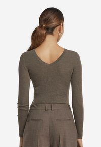 Brun ribbad långärmad topp med V-ringning, i kombination med skräddarsydda byxor med bälte och bakfickor.