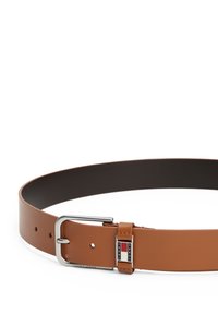 Cinturón de cuero marrón con una hebilla de metal plateado, que presenta un acento rectangular con el logotipo "TOMMY JEANS". Textura suave y múltiples agujeros de ajuste.